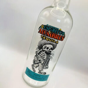A glass bottle of tequila with a label with a skeleton on it